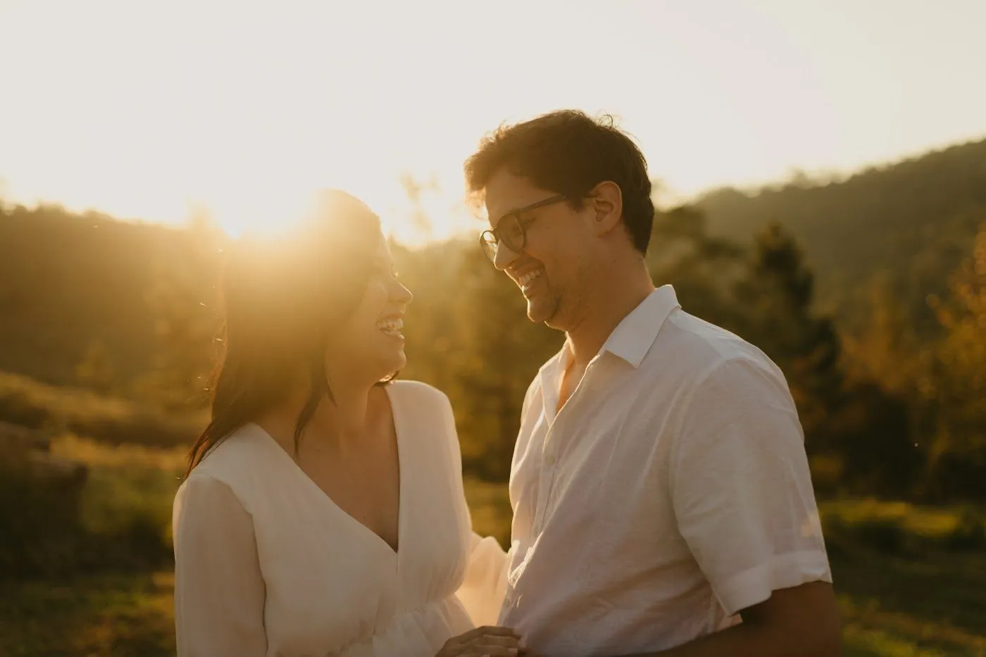 Natália e Douglas sorrindo um para o outro no ensaio pré-casamento, ao pôr do sol